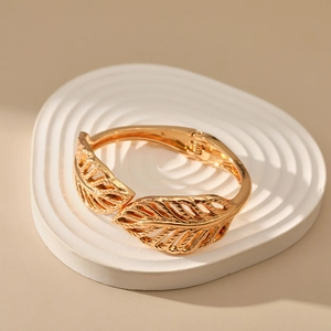 Detailed close-up of golden feather cuff bracelet with intricate hollow engraving