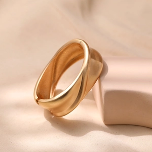 Macro detail of elegant matte gold crossover bangle with sleek layered geometric design