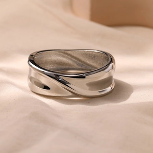 Macro detail of silver wave textured metal ring with polished finish on beige fabric