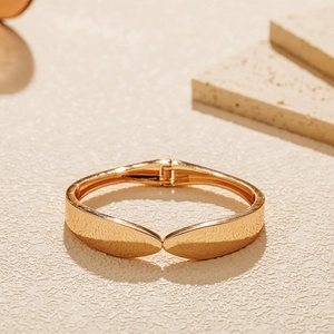 Detailed close-up of a minimalist gold-toned hinged bangle on textured travertine stones