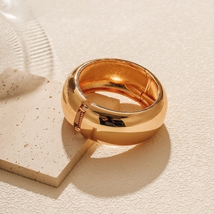 Detailed view of wide polished gold bangle resting on a beige stone slab textured background