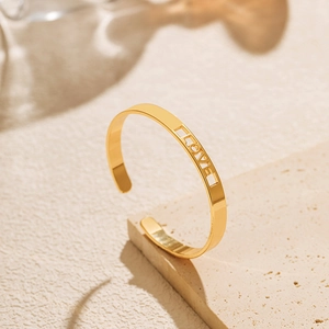 Detailaufnahme des goldenen Armreifs mit filigraner LOVE Gravur auf Stein-Hintergrund