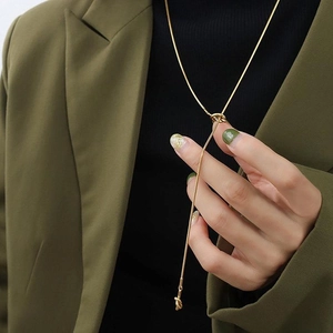 Macro detail of a long golden snake chain necklace worn over a dark turtleneck and blazer