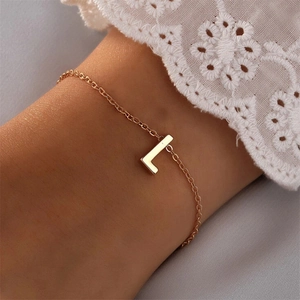 Bracelet doré minimaliste avec pendentif lettre L porté sur fond de dentelle blanche