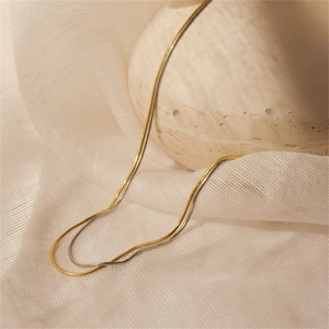 Detail of layered gold and silver snake chains on textured ceramic and mesh surface