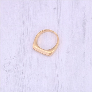 Close-up of minimalist gold plated square ring on light wood texture background
