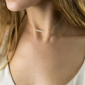 Elegant gold stainless steel necklace with five white pearls worn by a female model