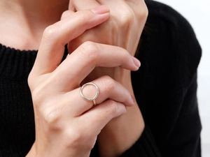 Primer plano de un anillo circular hueco plateado minimalista en el dedo de un modelo con fondo oscuro