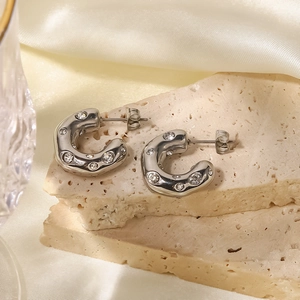 Detailed close-up of silver hammered C-shape earrings with zircon on a marble display