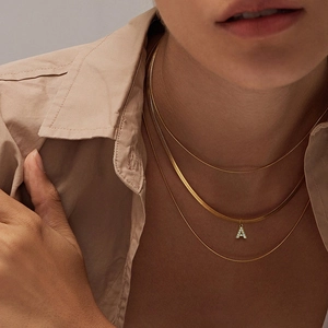 Detailed view of triple-layered gold snake bone necklaces with crystal A-letter pendant