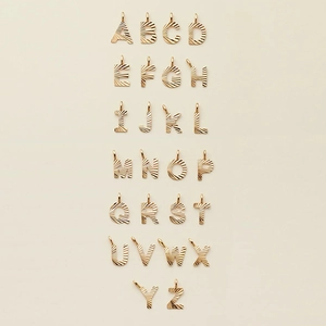 Set of 26 gold stainless steel alphabet pendants with radial texture on white background