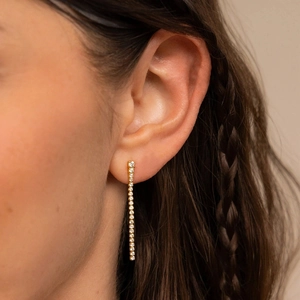 Boucles d'oreilles pendantes en or avec oxydes de zirconium portées par une femme