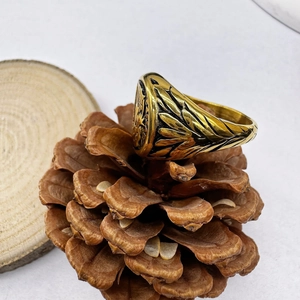 Close-up of golden Caesar ring with ornate feather engraving on a pine cone