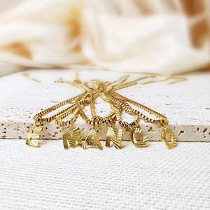 Detailed close-up of 14K gold plated letter pendants with radiant diagonal stripe texture