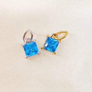 Detail of square blue zircon pendants in gold and silver settings on silk background
