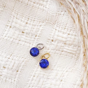 Macro shot of 7x7mm round faceted blue zircon pendants in gold and silver claw settings