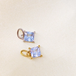 Macro shot of square blue zircon charms with four-prong settings in gold and silver