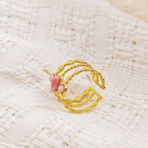 Detalle de anillo multicapa de acero dorado con piedras rosas sobre tejido blanco