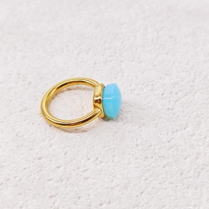 Detail of a minimalist gold ring with a faceted light blue gemstone on white fabric