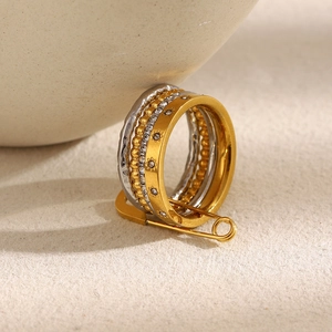 Detailed view of layered 18K gold and silver rings on a golden safety pin connector