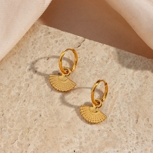 Detailed view of bohemian golden fan-shaped earrings with radial textures on marble base
