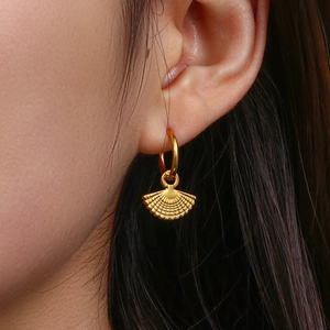 Close-up of a woman wearing gold bohemian fan-shaped earrings with fine beaded texture
