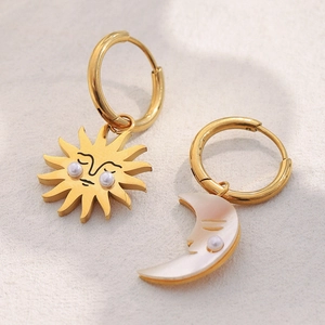 Macro shot of gold sun and pearl crescent moon mismatched drop earrings with faces
