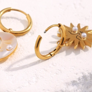 Detail view of gold 18K sun and moon earrings with pearls on a white stone background