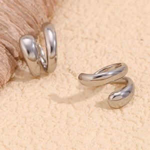 Detailed view of minimalist polished silver C-shaped double ear cuffs on a warm background