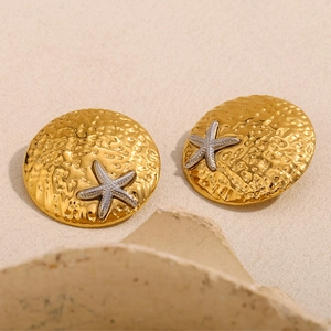 Detail shot of gold hammered round earrings with silver starfish accents on stone background