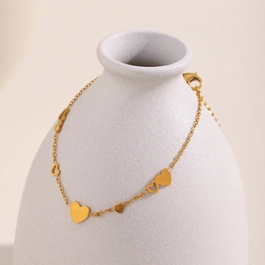 Détail d'un bracelet à breloques cœur en acier doré 18K sur un pot en céramique