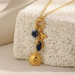 Detalle macro del collar chapado en oro 18K con colgantes de sol, abeja y esmalte azul