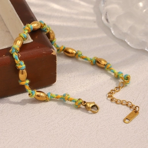 Détail d'un bracelet en corde colorée tressée avec des perles dorées sur surface texturée