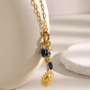 Detalle del collar con colgante de sol en oro de 18K y cuentas azules sobre cerámica