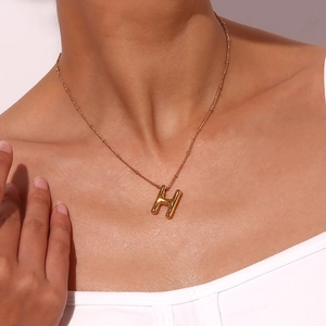 Detail van gouden ballon-stijl H-letter hanger aan een subtiele kralenketting