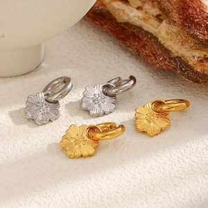 Macro shot of 18K gold and silver floral pendant hoop earrings on a stone texture