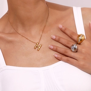 Detail van de 18K gouden ballon H ketting en pavé-gezette bolle ringen gedragen door model
