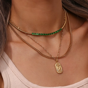 Close-up of triple-layered gold Pisces zodiac necklace set with green gems on a model