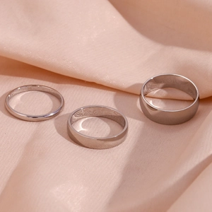 Three-piece set of polished silver stainless steel rings in varying widths on satin