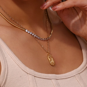 Close-up of layered gold Gemini zodiac pendant and snake chain necklace on a model