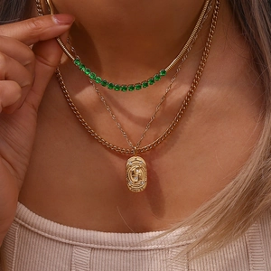 Close-up of layered gold zodiac necklaces including a Pisces coin pendant and green stones