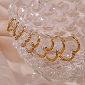 Close-up of four pairs of 18K gold plated minimalist hoop earrings on a glass edge