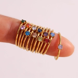Close-up of stacked thin gold rings set with various colorful birthstones on a finger