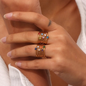 Detail of layered gold stainless steel rings with colorful rainbow birthstones on finger