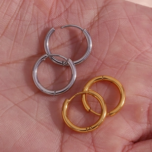 Close-up of gold and silver minimalist stainless steel hoop earrings held in palm