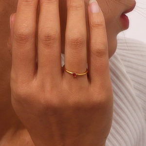 Close-up of a slim 18K gold plated stainless steel ring with a red birthstone on a finger