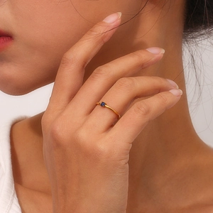 Close-up of minimalist gold thin ring with a single round blue stone on a model's hand
