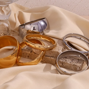 Close-up of minimalist polished gold and silver wide bangles on a textured stone surface