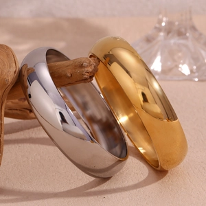 Polished chunky stainless steel bangles in gold and silver finish on a wooden branch