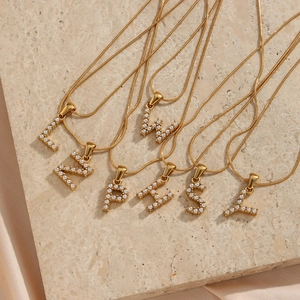 Λεπτομέρεια από επιχρυσωμένα κολιέ 18K με μενταγιόν γράμματα από πέρλες πάνω σε πέτρα
